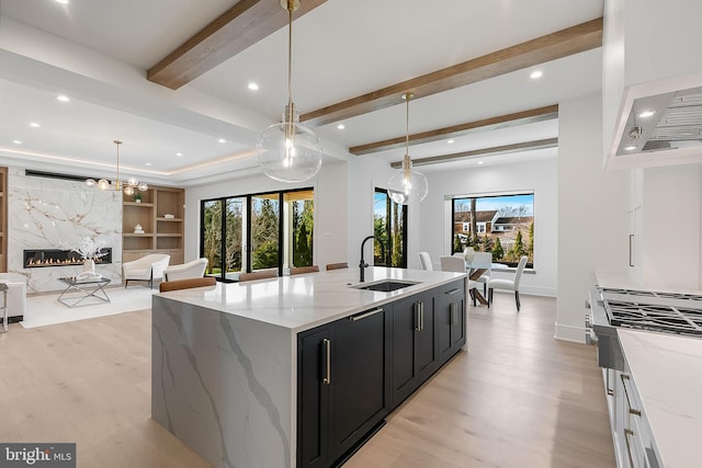 kitchen featuring pendant lighting, light stone counters, sink, and an island with sink