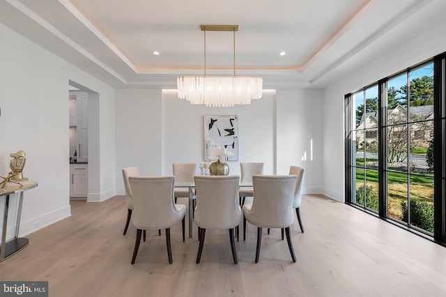 dining area featuring an inviting chandelier, light hardwood / wood-style flooring, and a tray ceiling