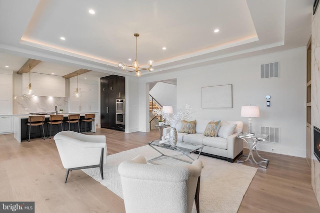 living room featuring a notable chandelier, light hardwood / wood-style floors, a raised ceiling, and a fireplace