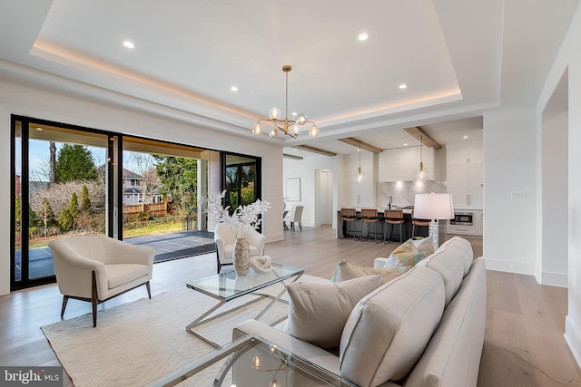 living room featuring a raised ceiling, sink, light hardwood / wood-style flooring, and a notable chandelier