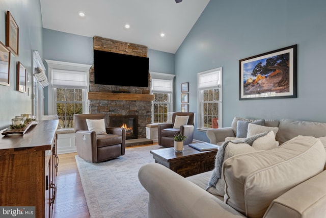 living room with light wood-type flooring, a wealth of natural light, a stone fireplace, and high vaulted ceiling