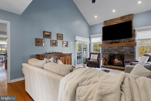 living room featuring hardwood / wood-style flooring, ceiling fan, high vaulted ceiling, and a stone fireplace