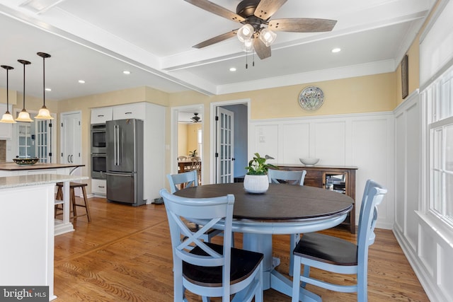 dining room with ceiling fan, light hardwood / wood-style floors, beam ceiling, ornamental molding, and french doors