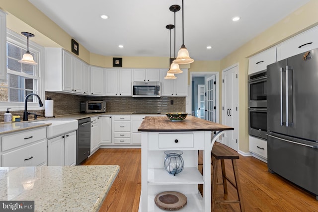 kitchen featuring a center island, hanging light fixtures, appliances with stainless steel finishes, white cabinets, and light stone counters