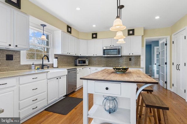 kitchen featuring a kitchen island, light hardwood / wood-style flooring, hanging light fixtures, appliances with stainless steel finishes, and white cabinets