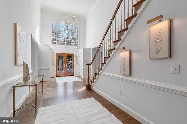 foyer with hardwood / wood-style flooring, a notable chandelier, french doors, a towering ceiling, and ornamental molding