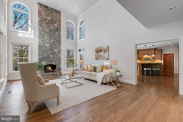 living room featuring a high ceiling, hardwood / wood-style flooring, crown molding, and a stone fireplace