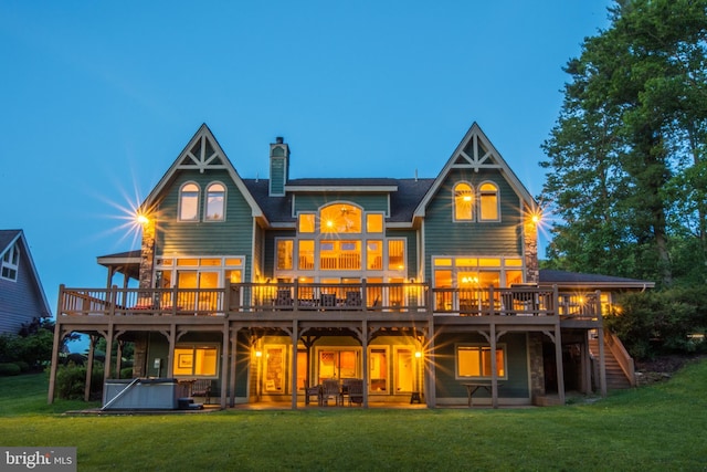 back house at dusk featuring a wooden deck, a patio area, a yard, and a hot tub