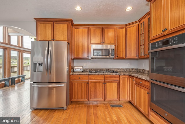 kitchen featuring appliances with stainless steel finishes, a textured ceiling, light hardwood / wood-style flooring, and dark stone counters