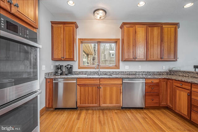 kitchen with sink, light hardwood / wood-style flooring, a textured ceiling, stone countertops, and stainless steel appliances