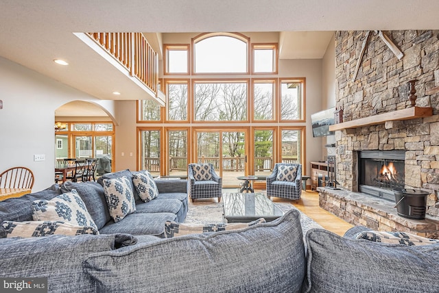 living room with a stone fireplace, a towering ceiling, and hardwood / wood-style flooring