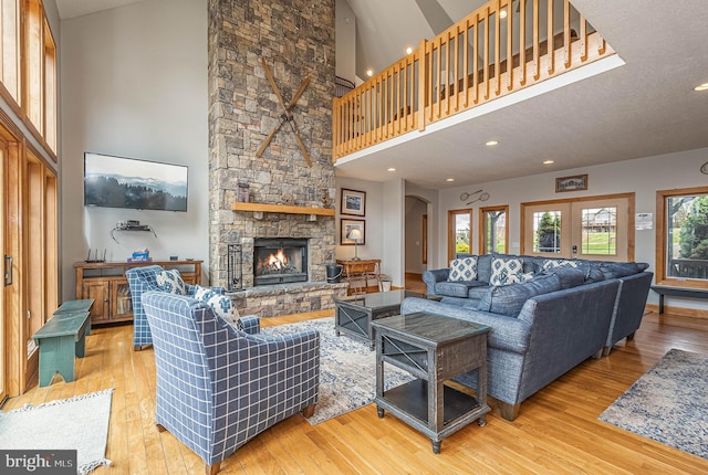 living room featuring light hardwood / wood-style floors, a stone fireplace, a textured ceiling, and a high ceiling