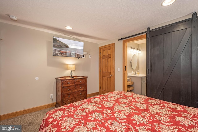 bedroom featuring carpet flooring, a textured ceiling, a barn door, and connected bathroom