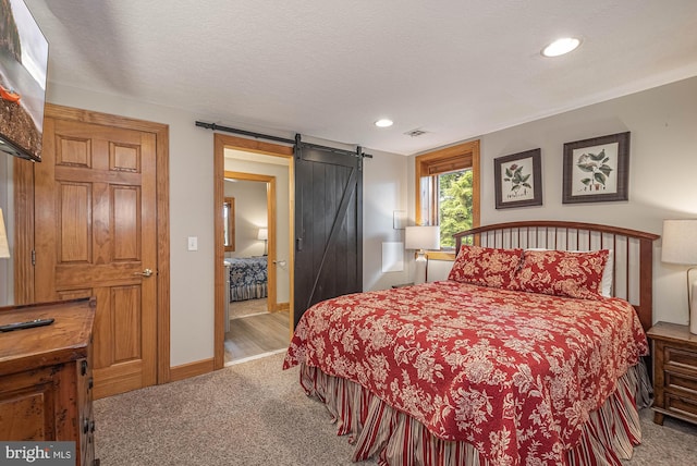 bedroom featuring a barn door, light carpet, and a textured ceiling