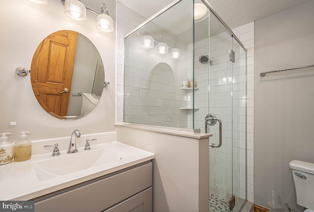 bathroom with vanity, toilet, a shower with door, and a textured ceiling