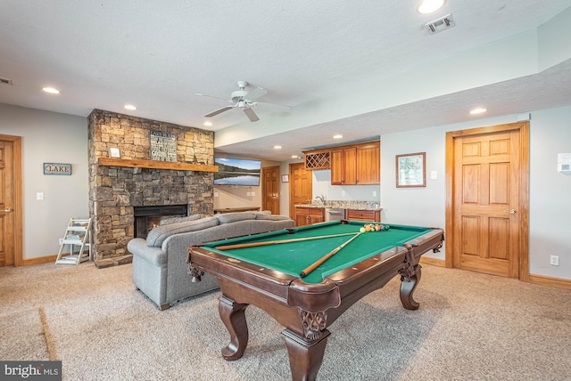 recreation room with a textured ceiling, light colored carpet, ceiling fan, a stone fireplace, and pool table