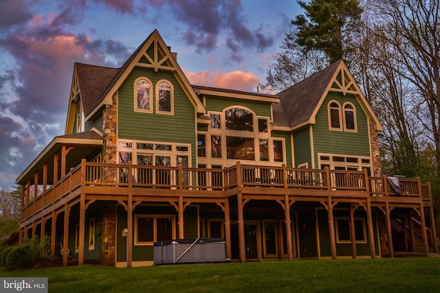 back house at dusk featuring a lawn, a wooden deck, and a hot tub