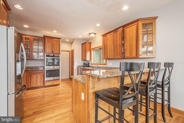 kitchen featuring a kitchen bar, a textured ceiling, appliances with stainless steel finishes, and light hardwood / wood-style flooring