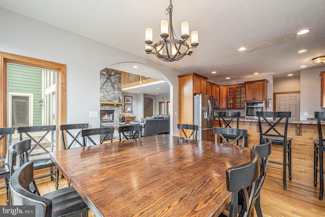 dining room with a fireplace, a textured ceiling, light hardwood / wood-style floors, and an inviting chandelier