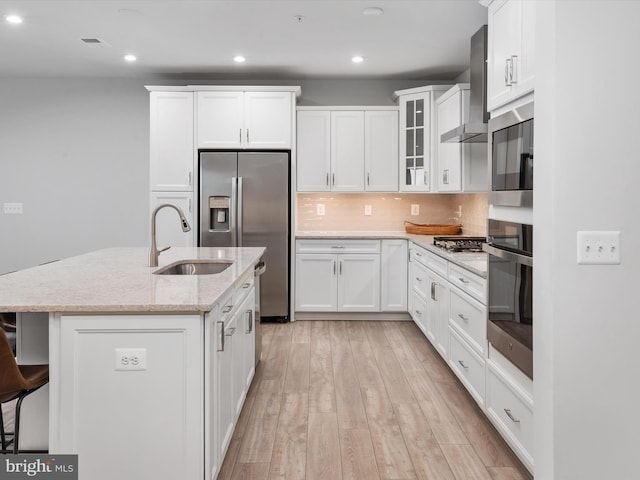 kitchen featuring stainless steel appliances, a sink, white cabinetry, wall chimney range hood, and light wood finished floors