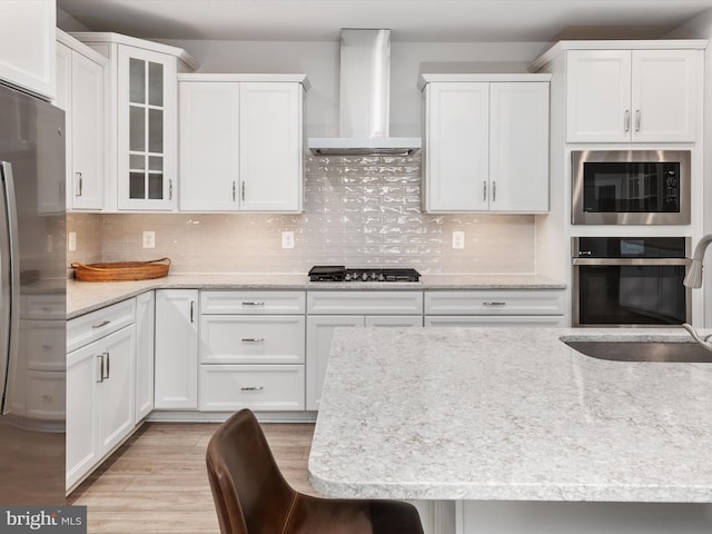 kitchen featuring white cabinetry, wall chimney exhaust hood, stainless steel appliances, and a kitchen bar