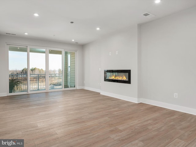 unfurnished living room featuring visible vents, baseboards, a glass covered fireplace, light wood-style flooring, and recessed lighting