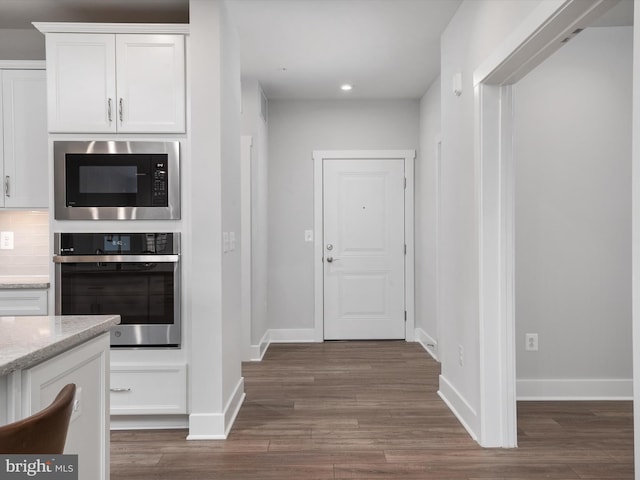 kitchen with built in microwave, stainless steel oven, white cabinets, and dark wood finished floors