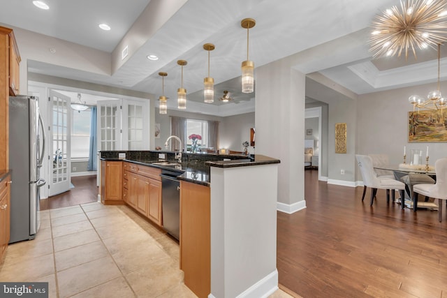 kitchen with a raised ceiling, a healthy amount of sunlight, dark stone countertops, light hardwood / wood-style floors, and stainless steel refrigerator