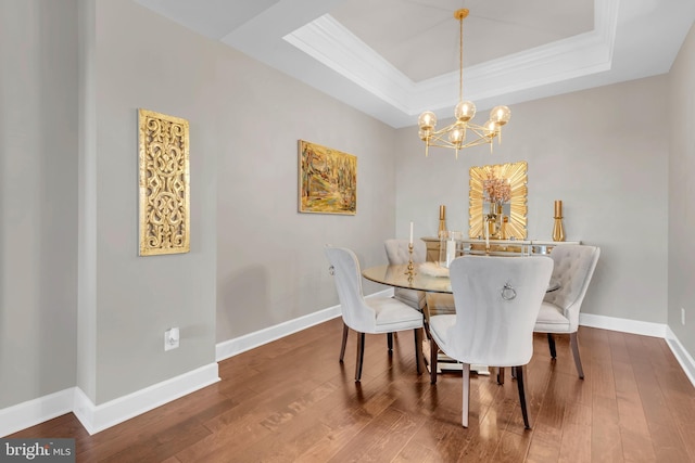 dining area with hardwood / wood-style flooring, a notable chandelier, ornamental molding, and a tray ceiling