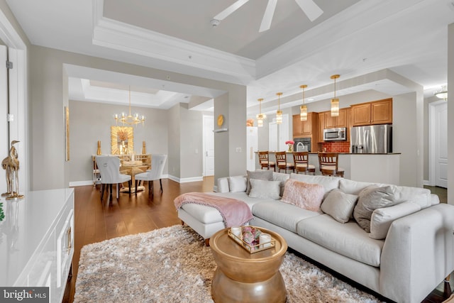 living room with a tray ceiling, dark wood-type flooring, ceiling fan with notable chandelier, and ornamental molding