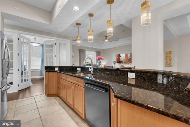 kitchen with stainless steel appliances, a raised ceiling, dark stone counters, decorative light fixtures, and light hardwood / wood-style floors