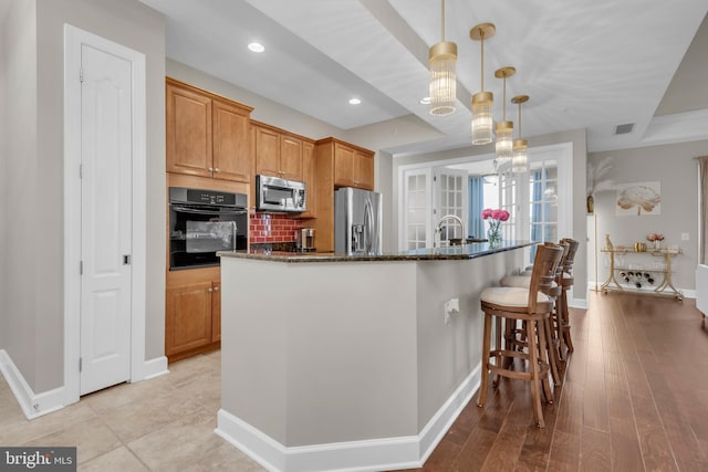 kitchen featuring appliances with stainless steel finishes, dark stone counters, pendant lighting, light hardwood / wood-style flooring, and an island with sink