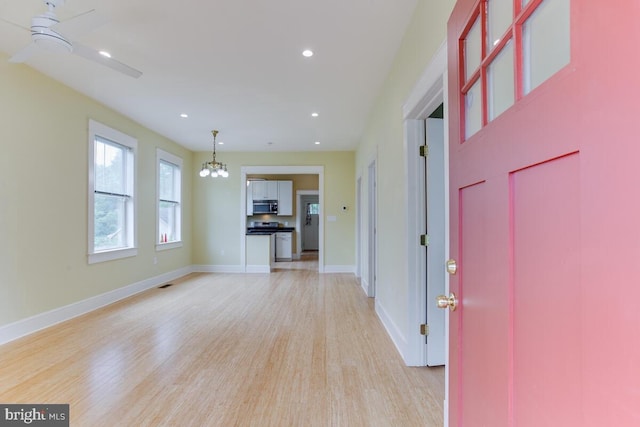 unfurnished living room with ceiling fan with notable chandelier and light hardwood / wood-style flooring