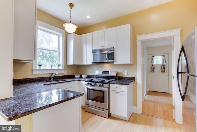 kitchen featuring sink, stainless steel appliances, pendant lighting, white cabinets, and light wood-type flooring