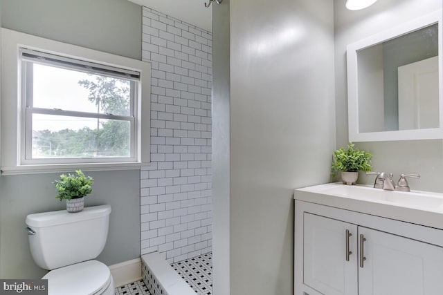 bathroom with tile patterned flooring, toilet, a tile shower, and vanity