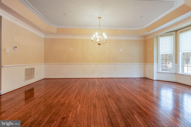 empty room featuring hardwood / wood-style floors, a raised ceiling, crown molding, and a notable chandelier