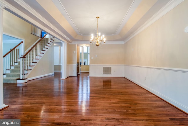 empty room featuring dark wood-type flooring, a chandelier, crown molding, and a tray ceiling