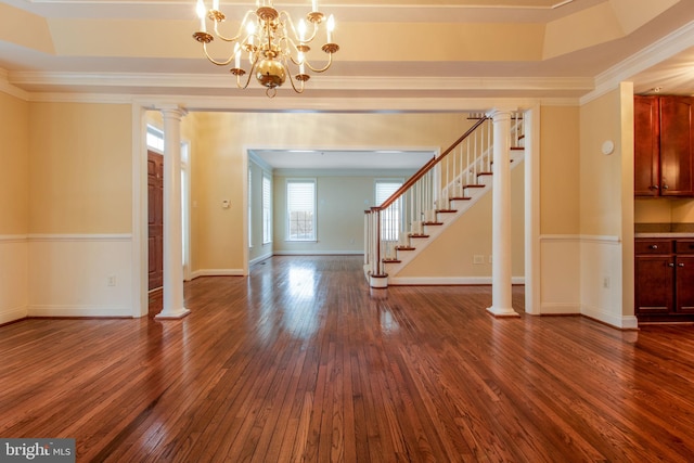 foyer featuring ornate columns, a tray ceiling, dark wood-type flooring, a chandelier, and crown molding