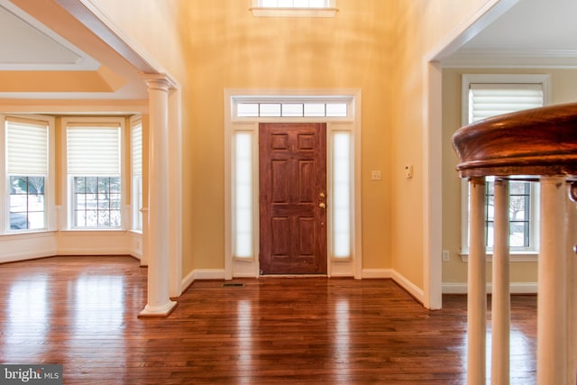 entrance foyer with decorative columns, dark wood-type flooring, a wealth of natural light, and ornamental molding