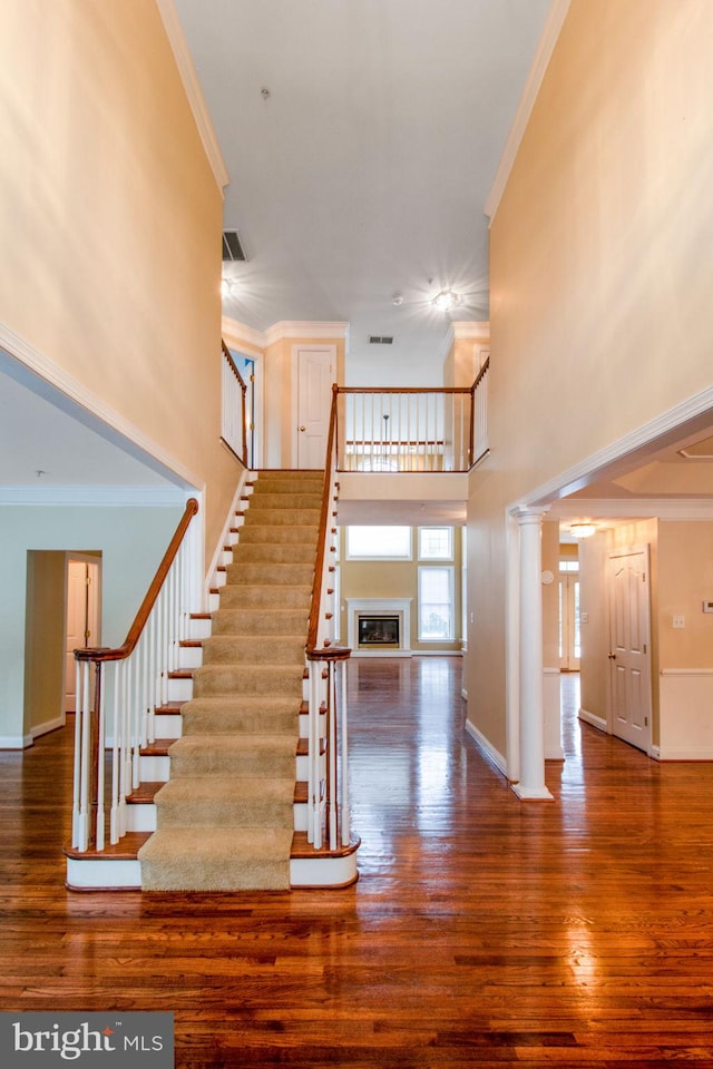 staircase with wood-type flooring, ornamental molding, and a towering ceiling