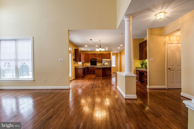 unfurnished living room featuring decorative columns, dark hardwood / wood-style floors, and a chandelier