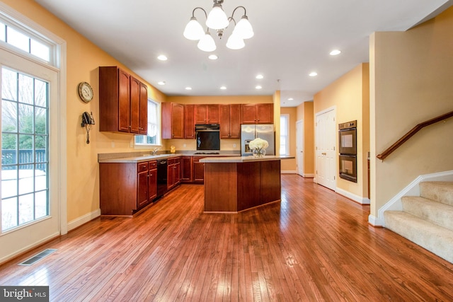 kitchen featuring decorative light fixtures, dark hardwood / wood-style floors, a center island, black appliances, and a chandelier