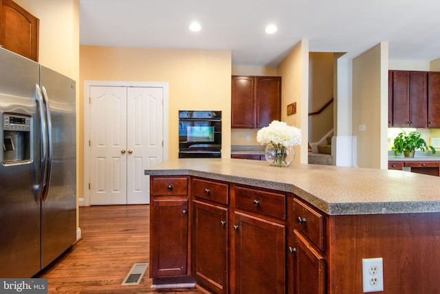 kitchen with light wood-type flooring, stainless steel refrigerator with ice dispenser, black oven, and a center island