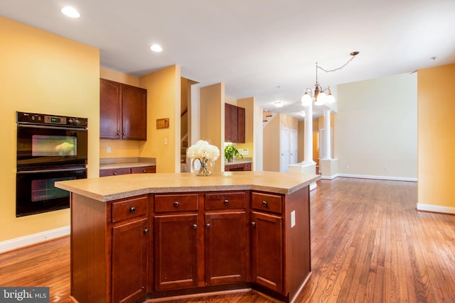 kitchen with black double oven, light hardwood / wood-style floors, a chandelier, and a kitchen island