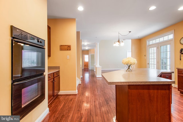 kitchen with ornate columns, an inviting chandelier, hardwood / wood-style floors, black double oven, and a kitchen island