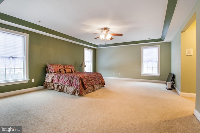 carpeted bedroom featuring ceiling fan and a tray ceiling