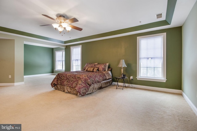 carpeted bedroom with ceiling fan, multiple windows, and a raised ceiling