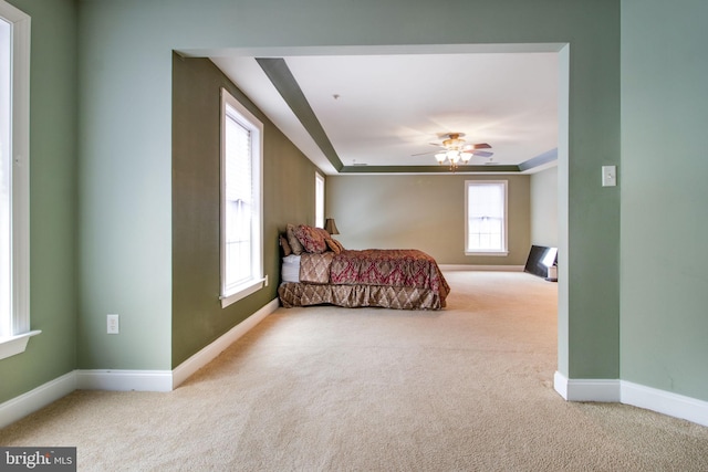 bedroom featuring ceiling fan, a raised ceiling, and light carpet