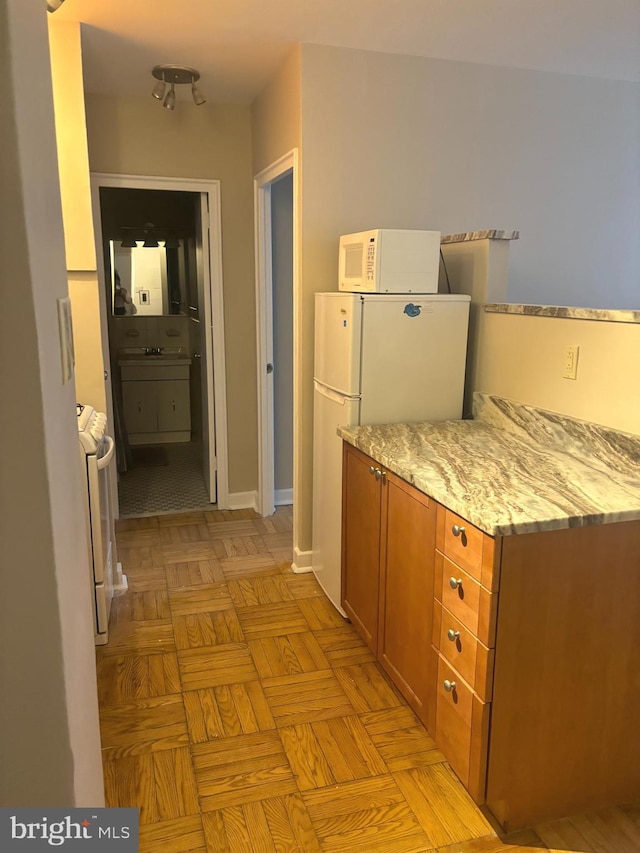 kitchen with sink, white appliances, light stone counters, and light parquet flooring