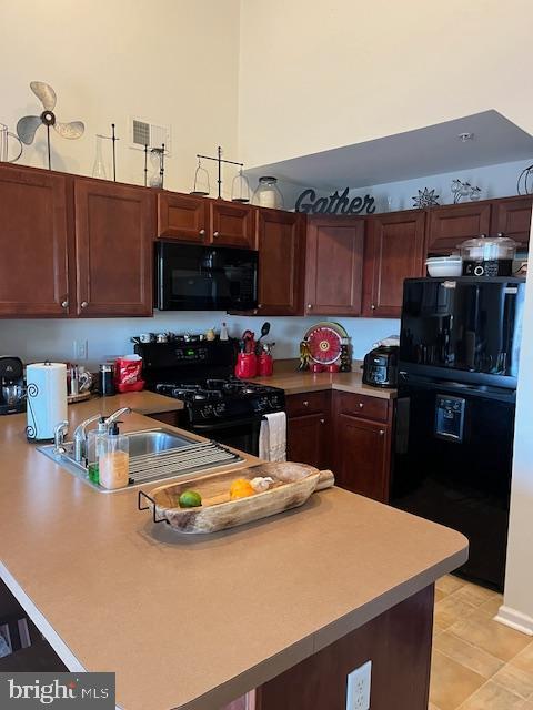 kitchen featuring black appliances, kitchen peninsula, light tile patterned floors, and sink